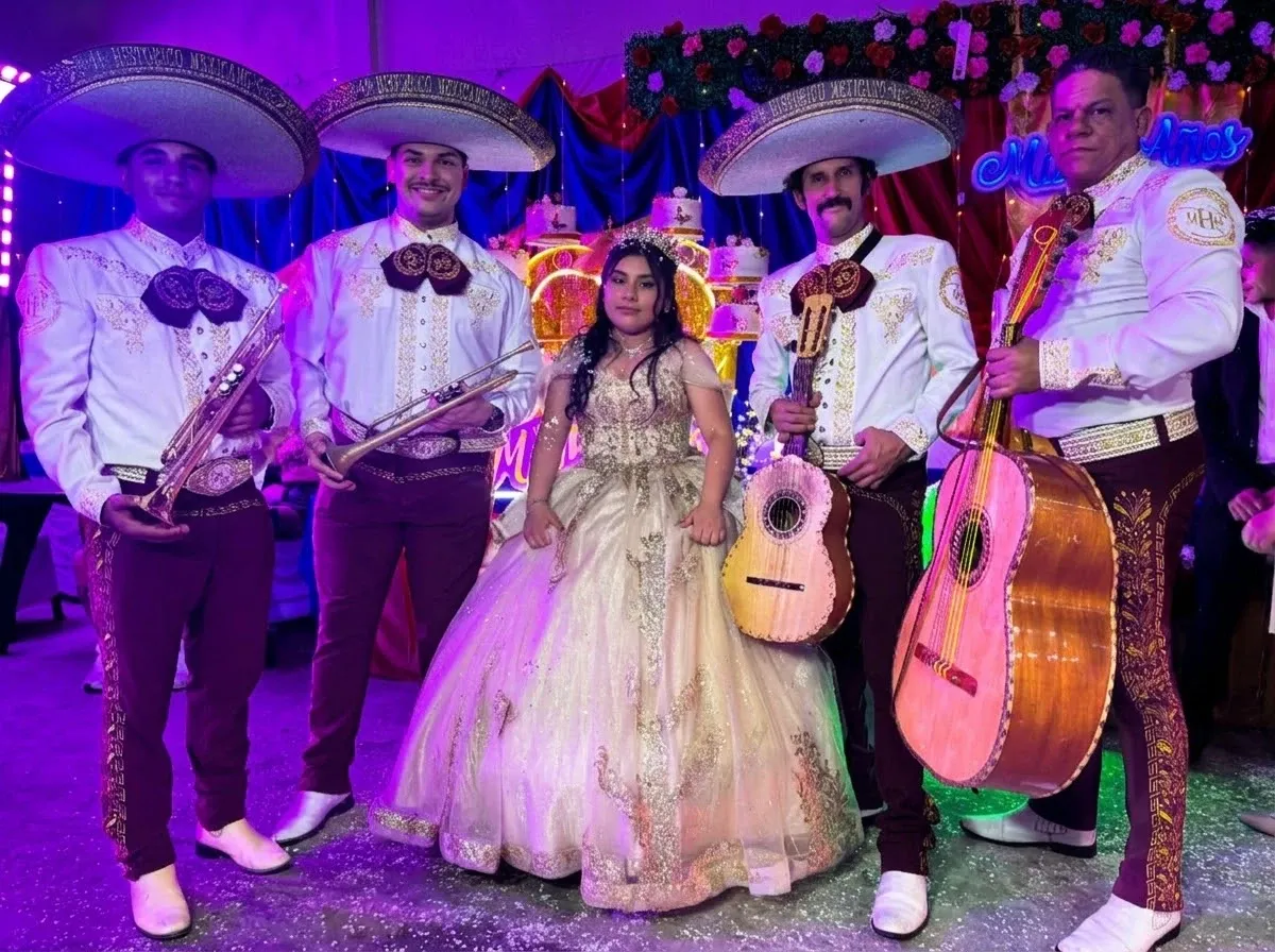 Cuatro mariachis con sombreros posan junto a una quinceañera con vestido dorado en su fiesta de 15